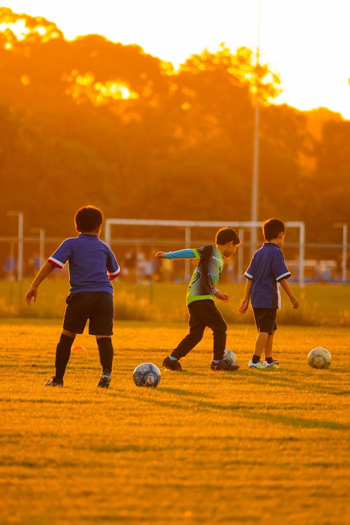 Three boys playing soccer on a grassy field at sunset, creating a warm and playful atmosphere.